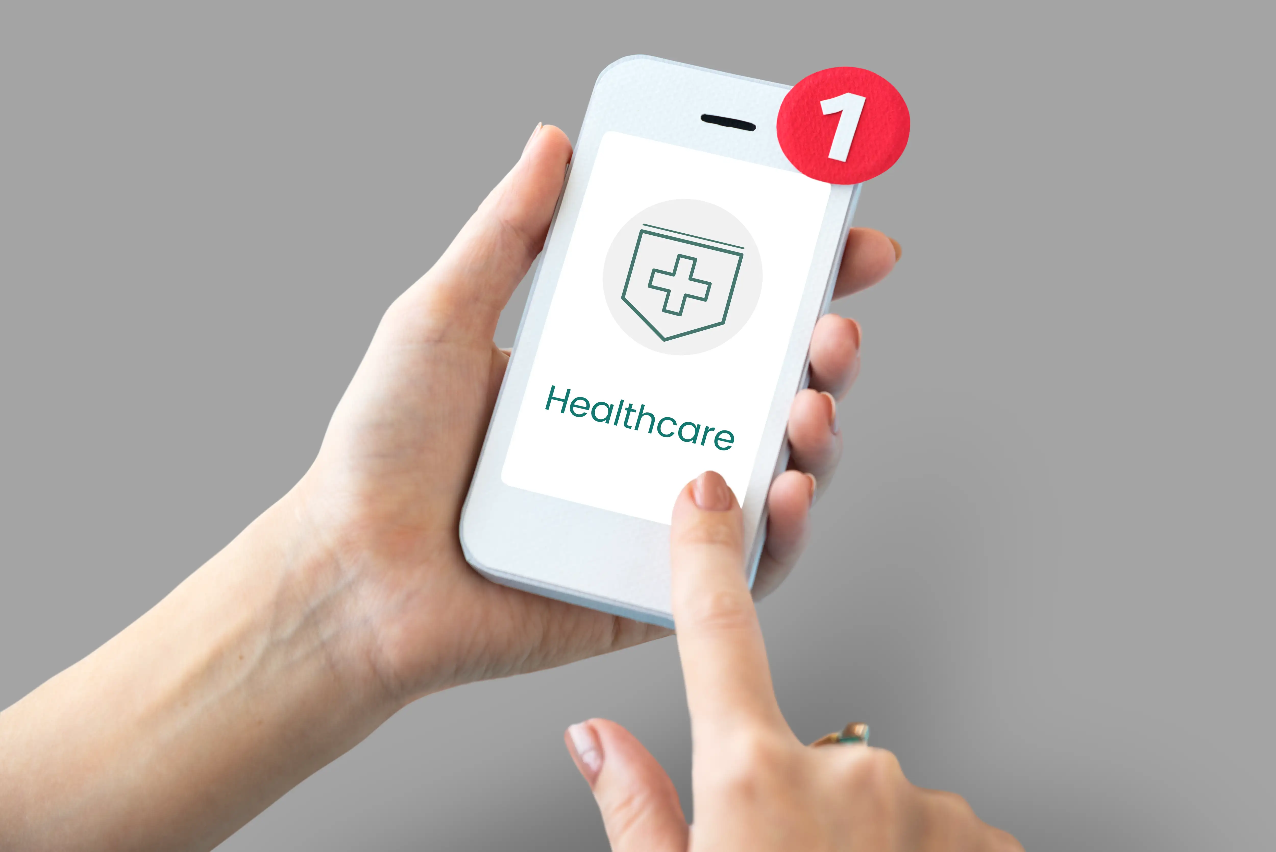 Hands holding white smartphone displaying healthcare app with medical cross shield icon and red notification badge showing one unread message for telemedicine and digital health services